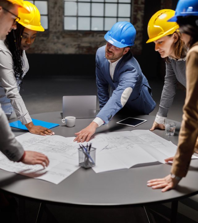 Group of building contractors cooperating while examining blueprints in the office.